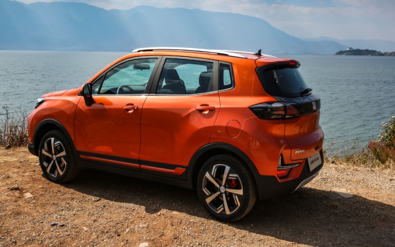 Changan CS15 naranja, vista trasera, estacionado en un mirador con un lago y montañas al fondo.